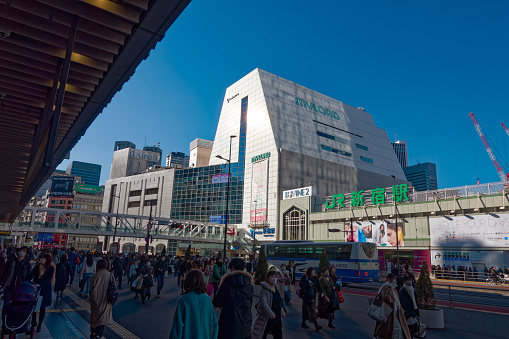 Train passengers at Shinjuku Station with shopping mall named Lumine 2 in the background at Japanese City of Tokyo on a sunny winter day. Photo taken January 27th, 2024, Shinjuku City, Tokyo, Japan.