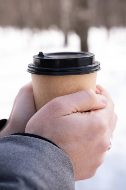 istock Male hands holding paper cup with coffee on snow background. 2137220012