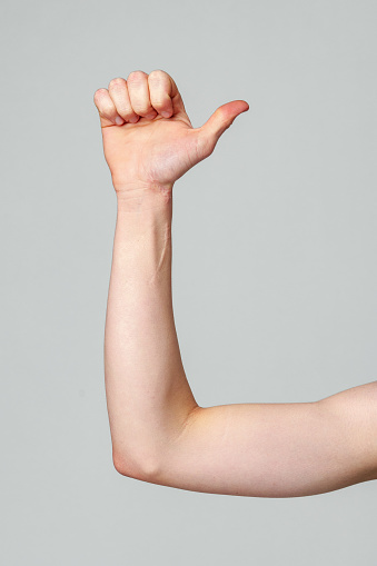 A close-up view of a persons forearm and hand raised against a neutral backdrop, with the thumb and index finger extended to form the letter L in American Sign Language, symbolizing non-verbal communication.