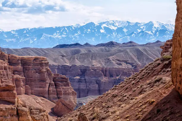 Photo of The huge Charyn Canyon in the desert of Kazakhstan. Panoramic view of a large canyon in the desert with mountains and snowy peaks on the horizon. Clouds in the sky