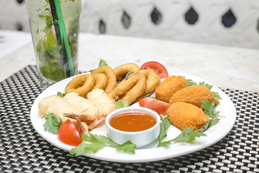 A white plate displays a delectable assortment of fried food, accompanied by a cup of rich and flavorful sauce.