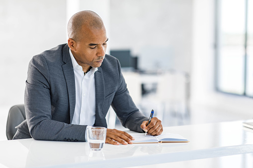 Mid adult black businessman writing down his plans while working in the office.