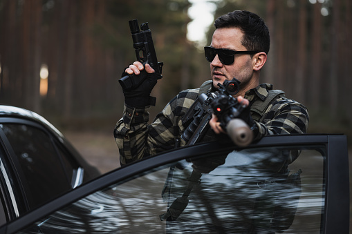 Private military man with a rifle with a silencer and a pistol near a car during tactical training. High quality photo