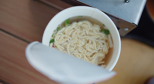 Overhead view of a cup of instant noodles being prepared with steaming hot water , a quick meal preparation