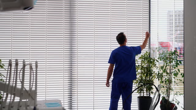 Healthcare worker looking through window blinds in clinic.