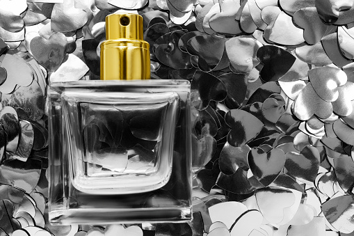 Transparent glass perfume bottle on silver metallic heart confetti background