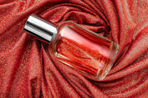 Transparent glass perfume bottle lying on red holographic draped fabric background