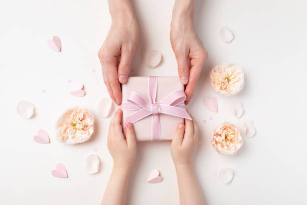 Child and mother holding a gift or present box decorated with flowers and hearts for Happy Mothers day. Holiday greeting top view.