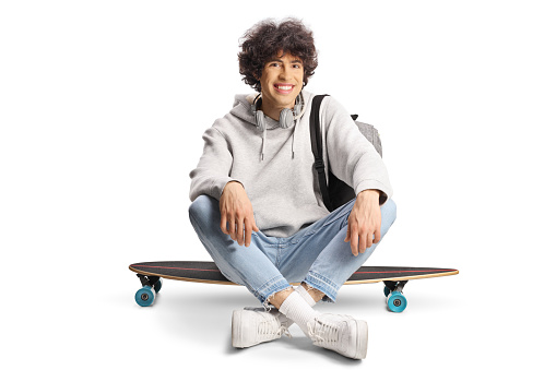 Male student sitting on a skateboard and smiling isolated on white background