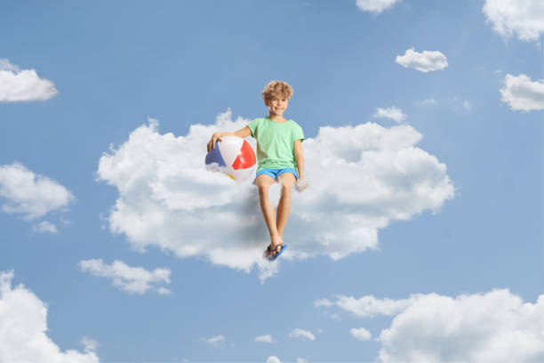 istock Boy with a beach ball sitting on a cloud 2137447220