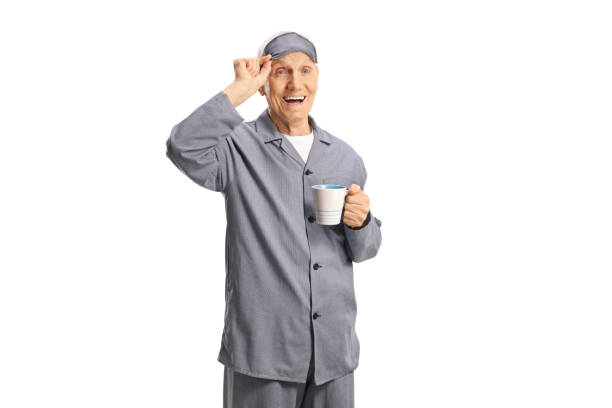 homme âgé en pyjama avec un masque de sommeil tenant une tasse - male mug shot cut out one person photos et images de collection