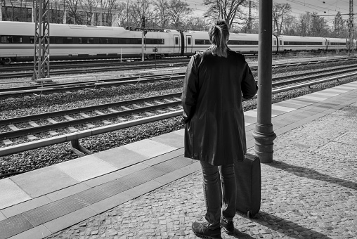 Germany, Berlin, March 26, 2024 -Rearview of woman standing with luggage at railroad station platform, Berlin Grunewald