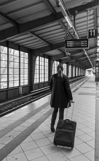 Germany, Berlin, March 26, 2024 - Rearview of woman standing with luggage at railroad station platform, Berlin Charlottenburg  Westkreuz