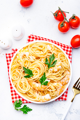 Spaghetti pasta with big shrimp, olive oil and parsley on white table background. Top view