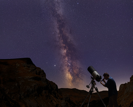 Man using a telescope and observing stars and the milky way on a night sky
