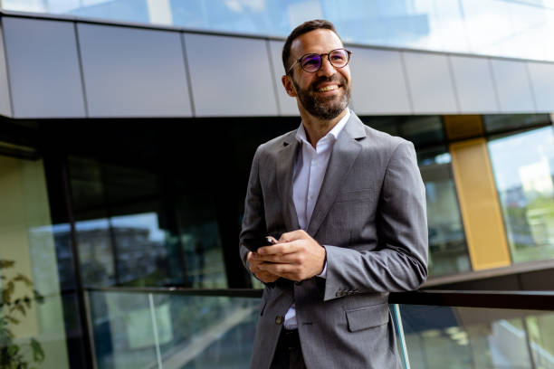 istock Confident Businessman Smiling in Sharp Suit Against Modern Glass Office Facade 2137493076