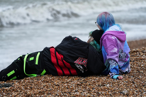 Brighton, Brighton And Hove, East Sussex, Southeastern England, United Kingdom, Britain, Europe - 16th March 2024: A couple lies on Brighton Beach, enjoying a peaceful moment together by the coast. The backdrop features the picturesque view of the English Channel and the Atlantic Ocean shoreline, complemented by the charming atmosphere of Brighton and Hove, located in East Sussex, England, United Kingdom.

Under a grey, overcast sky typical of an English winter day in Brighton, the gravel and pebble-strewn beachfront along the shore of the English Channel met the choppy waters of the Atlantic Ocean.

On the pebble and gravel shore of Brighton Beach, the two young British people sit along the beachfront, taking in the view of the choppy waters where the English Channel meets the Atlantic Ocean on this overcast English winter day.

This Brighton Beach in Brighton is a popular tourist destination, renowned for its diverse communities. Seaside.
