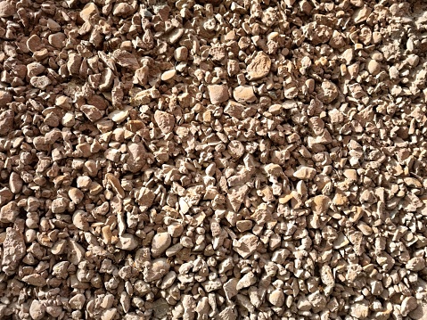 Sunlight illuminates a surface with small dirty brown pebbles. Stone background