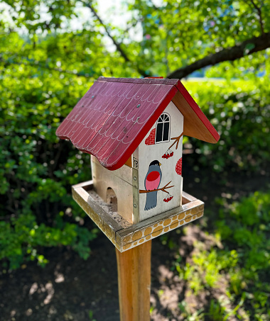 A hand-painted birdhouse with a vibrant red roof and illustrations of birds, perched outdoors with a lush green background