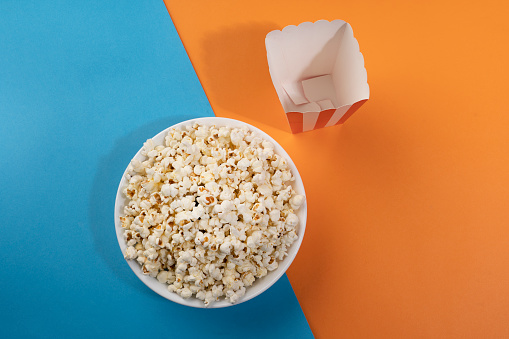 A bowl of popcorn and a box on a blue and orange background.