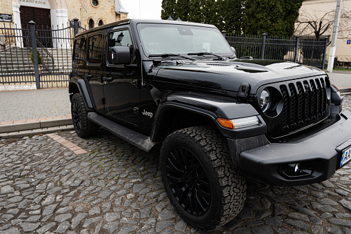 Lutsk, Ukraine - March, 2024: A high-end black Jeep Wrangler SUV showcasing its sleek design and rugged features, parked elegantly on a cobblestone city street.