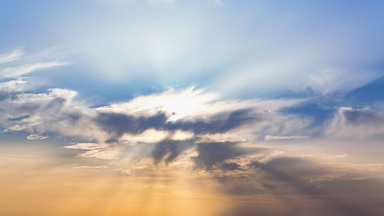 Serene sky scene with sun rays piercing through a central cloud, casting a warm glow on the surrounding clouds against a blue backdrop