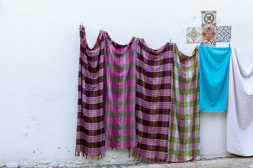 Clothes hang on a line against a white wall with decorative tiles, showcasing a vibrant plaid garment among others in a quaint setting. Kese dagi (old city) of Kusadasi, Turkiye (Turkey)