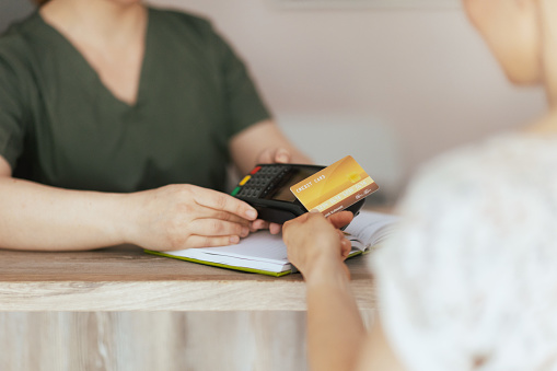 Healthcare time. Closeup on female massage therapist in massage cabinet with client accepting credit card payments via terminal on reception.