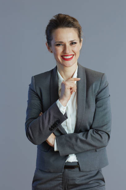 smiling young female worker in grey suit isolated on grey.