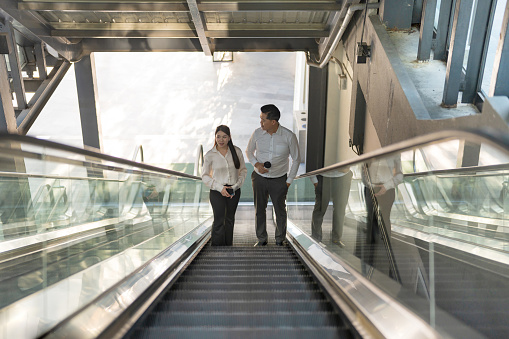 Professional business colleagues having a conversation while commuting on a modern escalator in the urban city environment in their white collar office attire