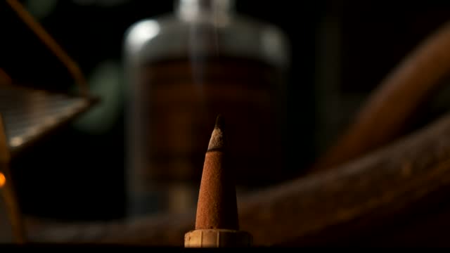 Close up of a incense cone burning with smoke spreading in a dark esoteric setting, in slow motion