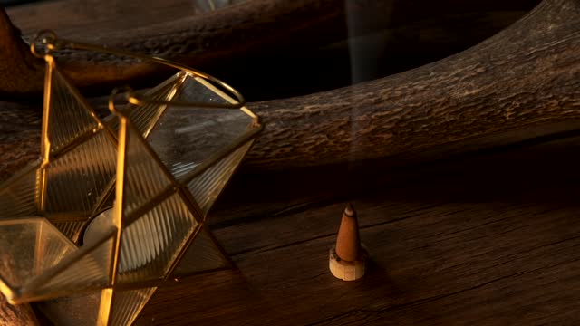 View of a incense cone burning with smoke and star shaped candle in a dark esoteric setting, in slow motion