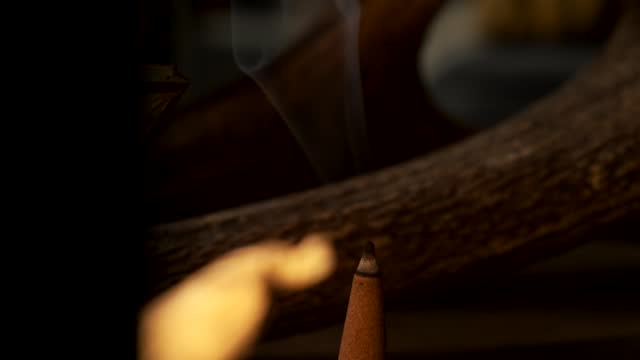 Close up crane shot of a incense cone burning with smoke in a dark esoteric setting, in slow motion