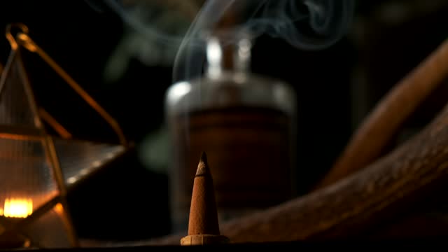 Detail view of a incense cone burning with smoke in a dark esoteric setting, in slow motion