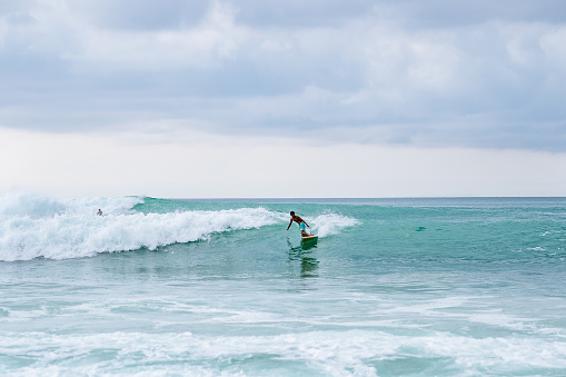 Bali, Dreamland beach - A surfer, balanced on a surfboard, rides a turquoise wave. Blue ocean in the background.