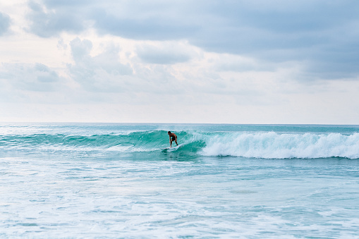 Bali, Dreamland beach - A surfer, balanced on a surfboard, rides a turquoise wave. Blue ocean in the background.