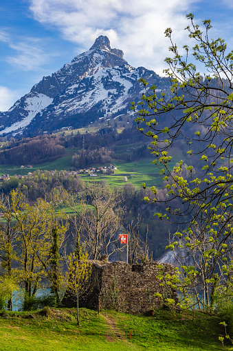 Betlis, Switezrland - April 17, 2022: The Ruin Stralegg with Swiss flag and the Muertschenstock mountain peak at the background