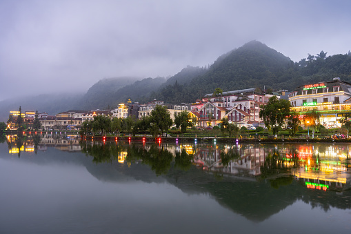 A scenic view of Sa Pa Lake in Vietnam enveloped in mist, with glowing buildings along the shore.