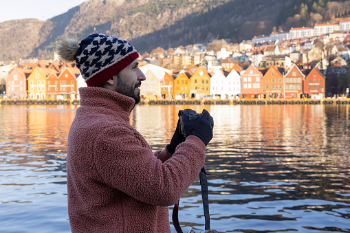 A male photographer frames the colorful houses of Bryggen by the waterfront.