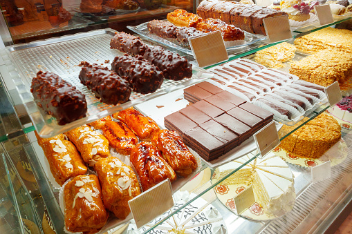 An array of freshly baked pastries and sweets temptingly showcased behind the glass display of a bakery shop. The selection includes cookies, cakes, and other confections that promise a treat for the taste buds.