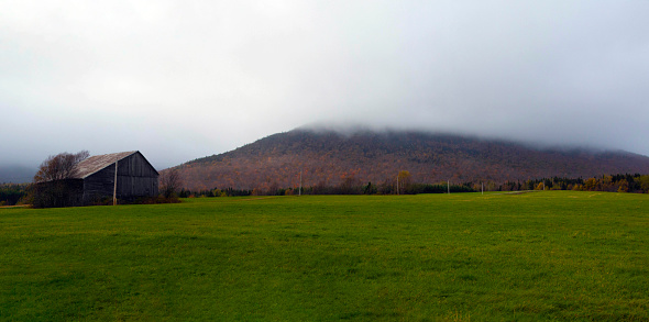 A barn in front of a misty mountain in a field.