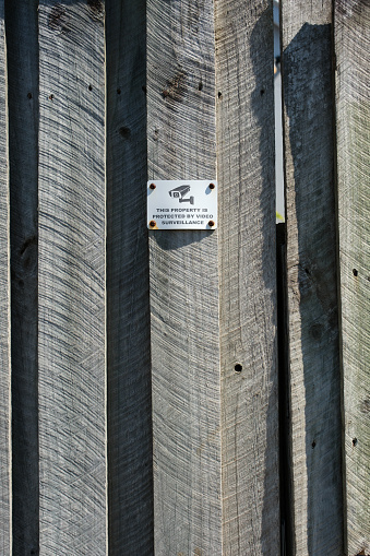 Old metal security camera sign on a wooden fence.