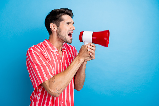 Photo of angry furious guy wear red shirt shouting loud speaker empty space isolated blue color background.