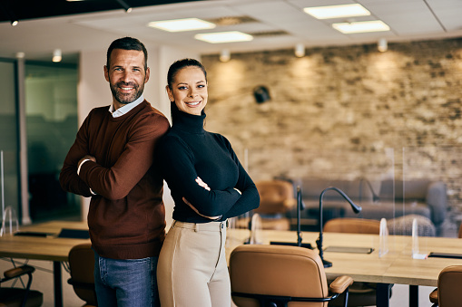 Two smiling business partners standing with hands crossed, posing at the office.