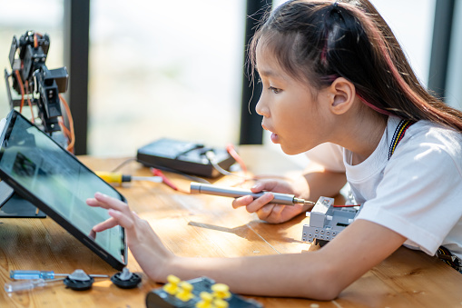 Smart young girl learns with small tools and assembles a robot kit while following instructions from a tablet computer. technology concept
