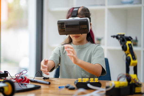 istock Young girl wearing a VR headset sits on a table moving her hands around. to work on assembling virtual robots ,technology concept 2137782095