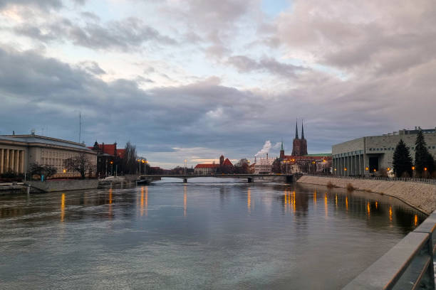 Wroclaw, Poland, February 15, 2024: A river flows through a bustling city, surrounded by towering skyscrapers and high-rise buildings. The urban landscape is juxtaposed with the movement of the flowing water, creating a striking scene of man-made structures intertwined with nature.