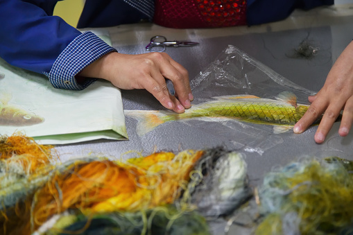 Hands of an embroiderer over canvas with exotic fish close up