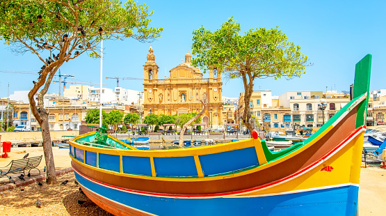 Maltese traditional colorful boat and Msida Parish Church on a background, Malta travel photo