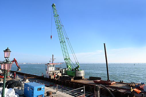 Venice, Italy, march 12, 2024 : Construction crane on a barge for renovation work on a quay in Venice